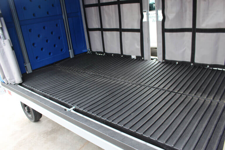 Close-up of black V-style floor inside a blue baggage cart with gray curtains.