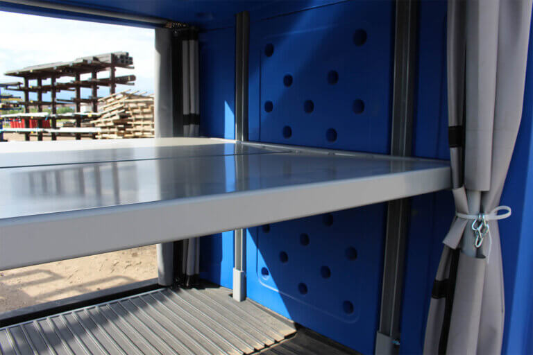 Interior view of blue baggage cart showing metal shelf, floor, and side curtains.