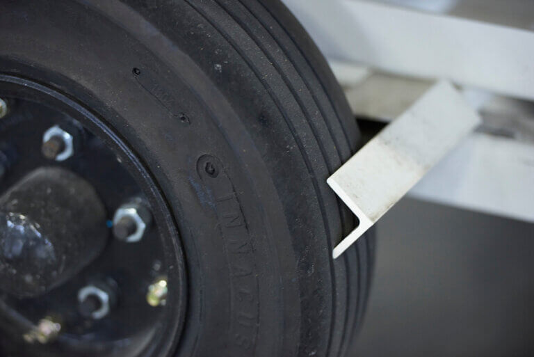 Close-up of industrial wheel showing metal brake lever pressed against black rubber tire with mounting hardware visible.