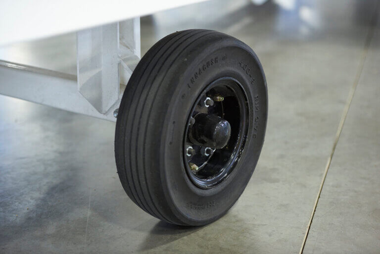 Close-up of black industrial pneumatic tire with ribbed tread pattern mounted on steel rim with lug nuts attached to aluminum frame.