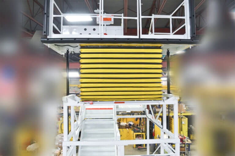 Industrial elevated work platform with yellow accordion mechanism, white safety railings, and spiral box stairs for access.