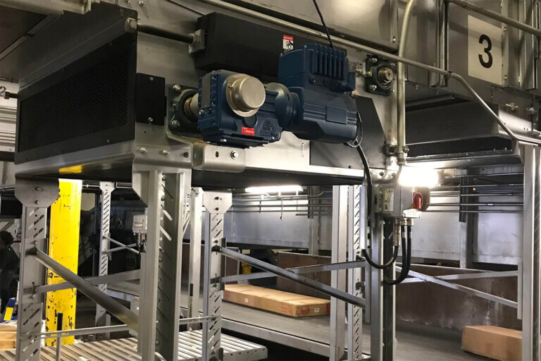 Blue industrial motor mounted on steel framework above a package conveyor system in a warehouse facility.
