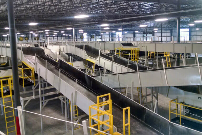 Elevated conveyor belt system with multiple inclined tracks and yellow safety railings in a warehouse setting.