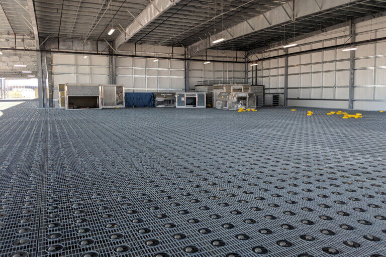 Large warehouse with metal grid flooring containing hundreds of integrated roller mechanisms for heavy material handling.