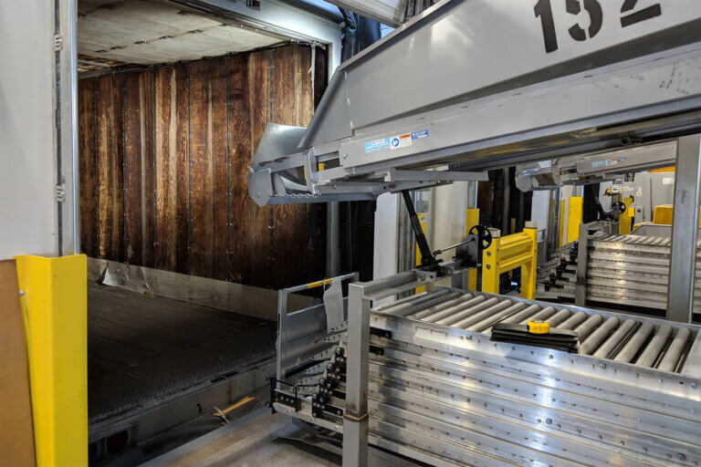 Industrial roller conveyor system with loading mechanism extending into a wooden-walled shipping trailer.