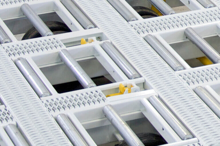White cargo trailer floor with metal rollers, perforated walking surfaces, and yellow indexing pins positioned between roller sections.