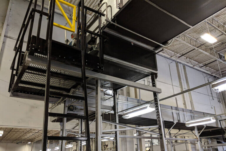 Elevated black metal maintenance platform with ladder and yellow safety gate installed near the ceiling of an industrial building.