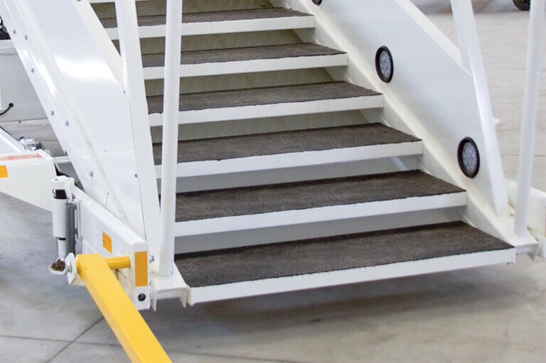 White metal industrial staircase with black non-slip treads and yellow safety features at the base.