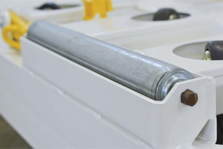 Metal cylindrical roller mounted in white housing with visible fastener and yellow components in background.