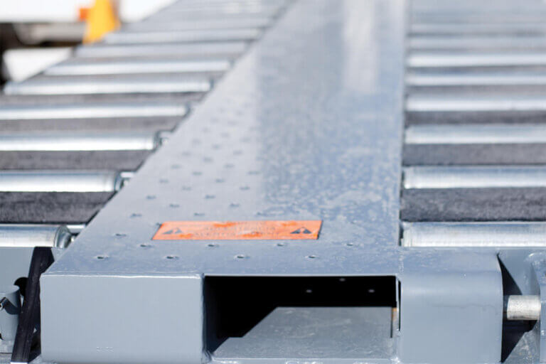 Metal platform with parallel roller tracks and forklift entry channels featuring orange safety markings.