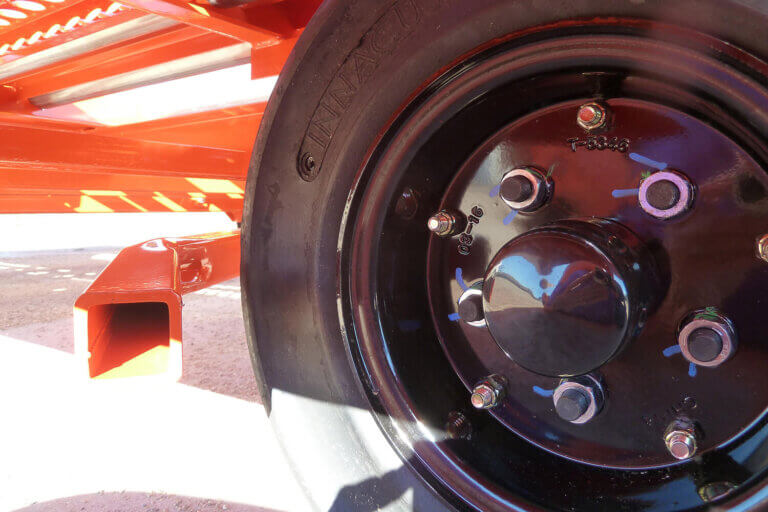 Close-up of black wheel hub with lug nuts on industrial trailer with bright orange frame.
