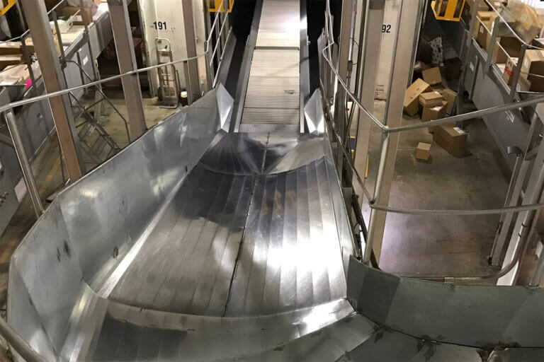 Metal package chute with conveyor belt between numbered sorting stations in a distribution facility.