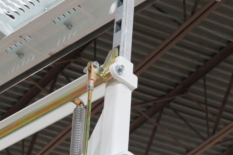 Close-up of hydraulic tension spring mechanism connecting white metal frame components for industrial stair system.