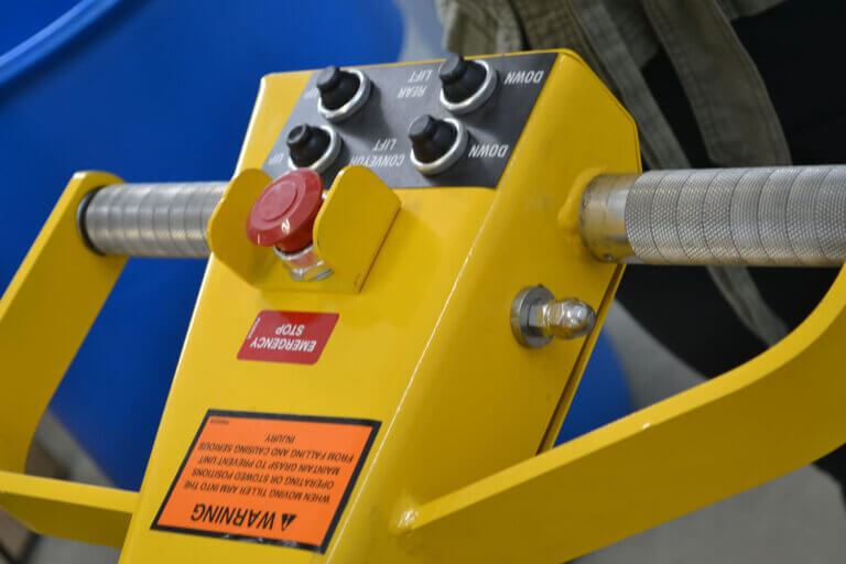 Yellow industrial control box with four black adjustment knobs, emergency stop button, and warning labels mounted on metal handle.