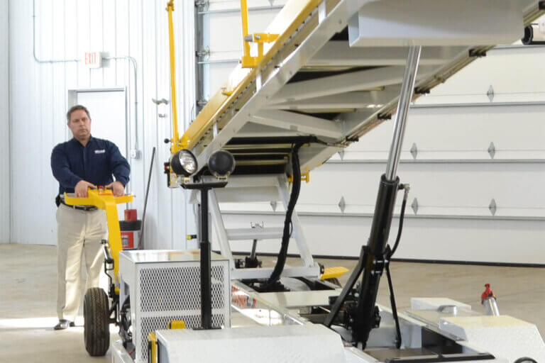 Warehouse worker operating a yellow and white walk-behind belt loader in an industrial facility.