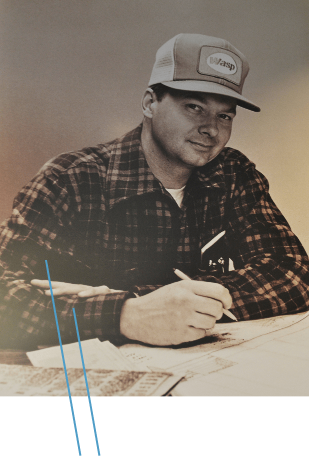 Person in plaid shirt and trucker cap writing on technical drawings.