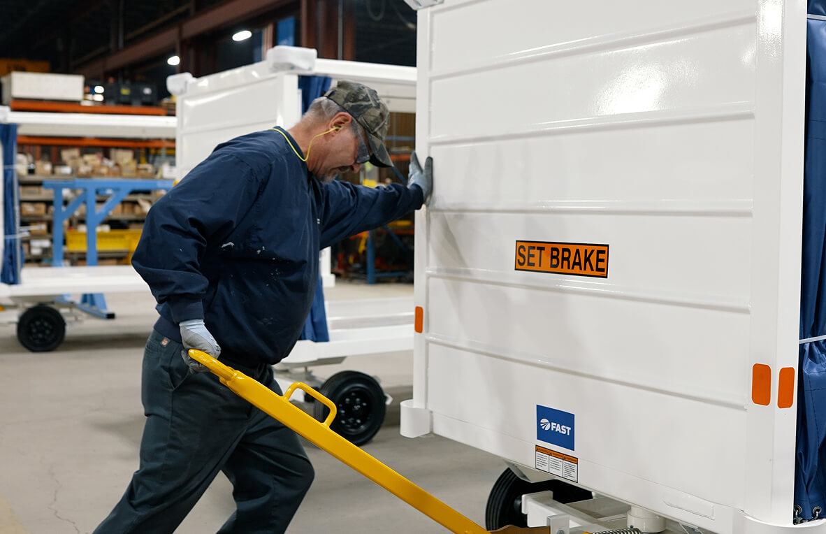 Factory worker in blue coveralls using a yellow towbar to position a white cart.