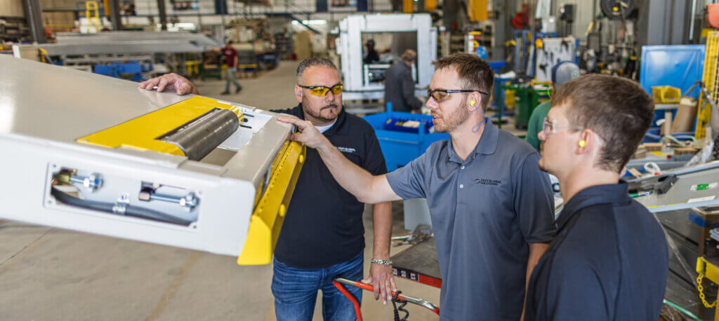 Manufacturing team members inspecting industrial equipment with yellow safety components in a factory setting.