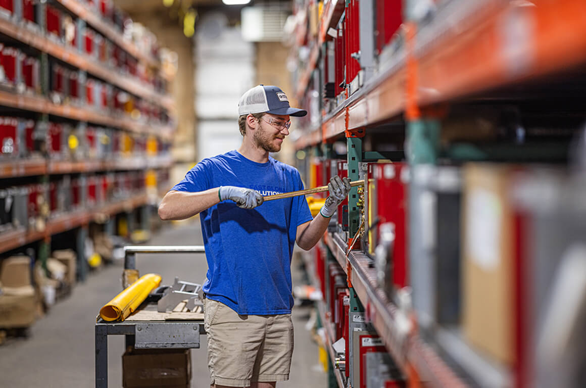 Worker in blue shirt and cap accessing parts on warehouse storage shelves.