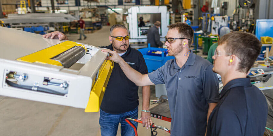 Manufacturing team members inspecting industrial equipment with yellow safety components in a factory setting.